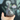 A hand holds the small, gray Baby Elephant Sherlock Pipe, viewed from a slightly upward angle against a blurred green background.