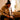 Side view of a seated person inhaling from a tall Glasscity Beaker Ice Bong with Double Tree Perc-Blue amid soft indoor light.