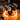 Front-facing shot of the DankStop Maria Ring Sherlock Pipe resting on a wooden table circled by low orange flames with smoke rising against a blurred striped blanket background