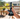 Handheld view of an Eyce Silicone Mini Beaker in jungle-patterned black and gray held outdoors on a sunny deck with blurred patio furniture and plants in the background
