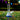 Close-up, low-angle view of the DankStop Big Base Beaker with Color Accents Bong - Green - 12 in. centered on grass with colorful confetti and blurred pennant flags in the background.