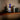 Center-front view of the DankStop Straight Tube Colored Glass Bong | Blue on a wooden shelf between a dark vase and stacked books, lit with soft side light.