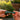 Two hands exchanging a shimmering iridescent LA Pipes Galactic Storm Full Dichro Spoon Pipe held horizontally against a sunlit blurred garden background.