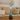 Close-up frontal view of the My Bud Vase "Mermaid" Ocean Goddess Bong showing its turquoise-green mermaid-tail neck, cream tail-fluke rim, and decorative blue sprig against a blurred sofa backdrop