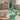 Front three-quarter view of the Aqua Teal Ooze Echo 4-in-1 Silicone Bong sitting on a wooden table in front of a blurred sofa and book.