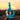Handheld against a soft sunset, the Ooze Echo 4-in-1 Silicone Bong in rasta-colored teal-blue is shown in three-quarter view highlighting its curved clear neck and textured silicone body.